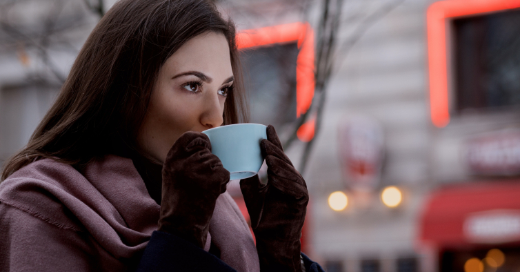 Jovem mulher com roupas quentes na neve fria do inverno bebendo café para  ir